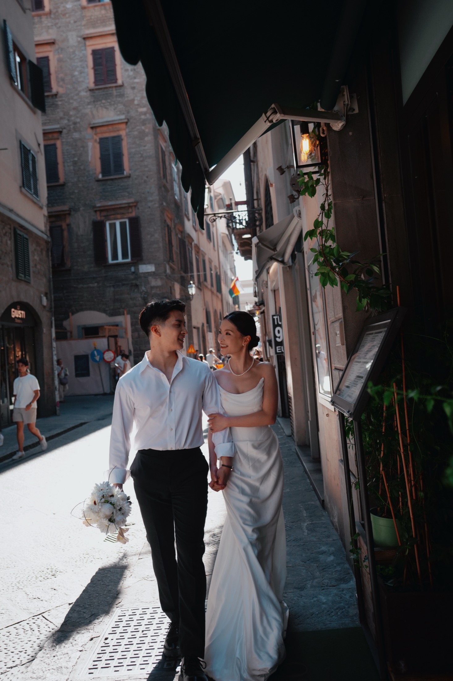 Yue and Andrew walking arm in arm down a narrow sunlit street