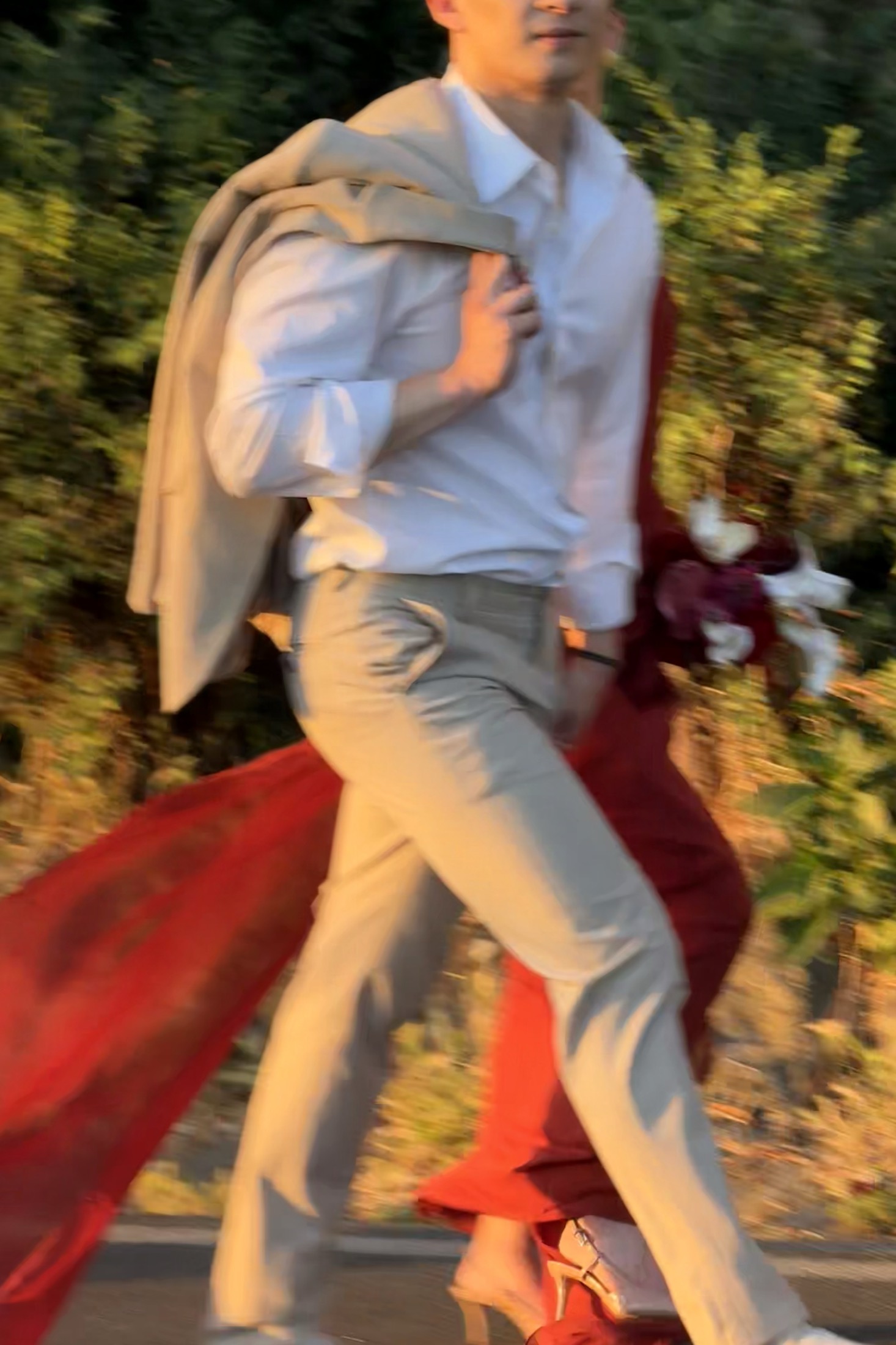 Yue and Andrew walking at golden hour, her red dress trailing behind