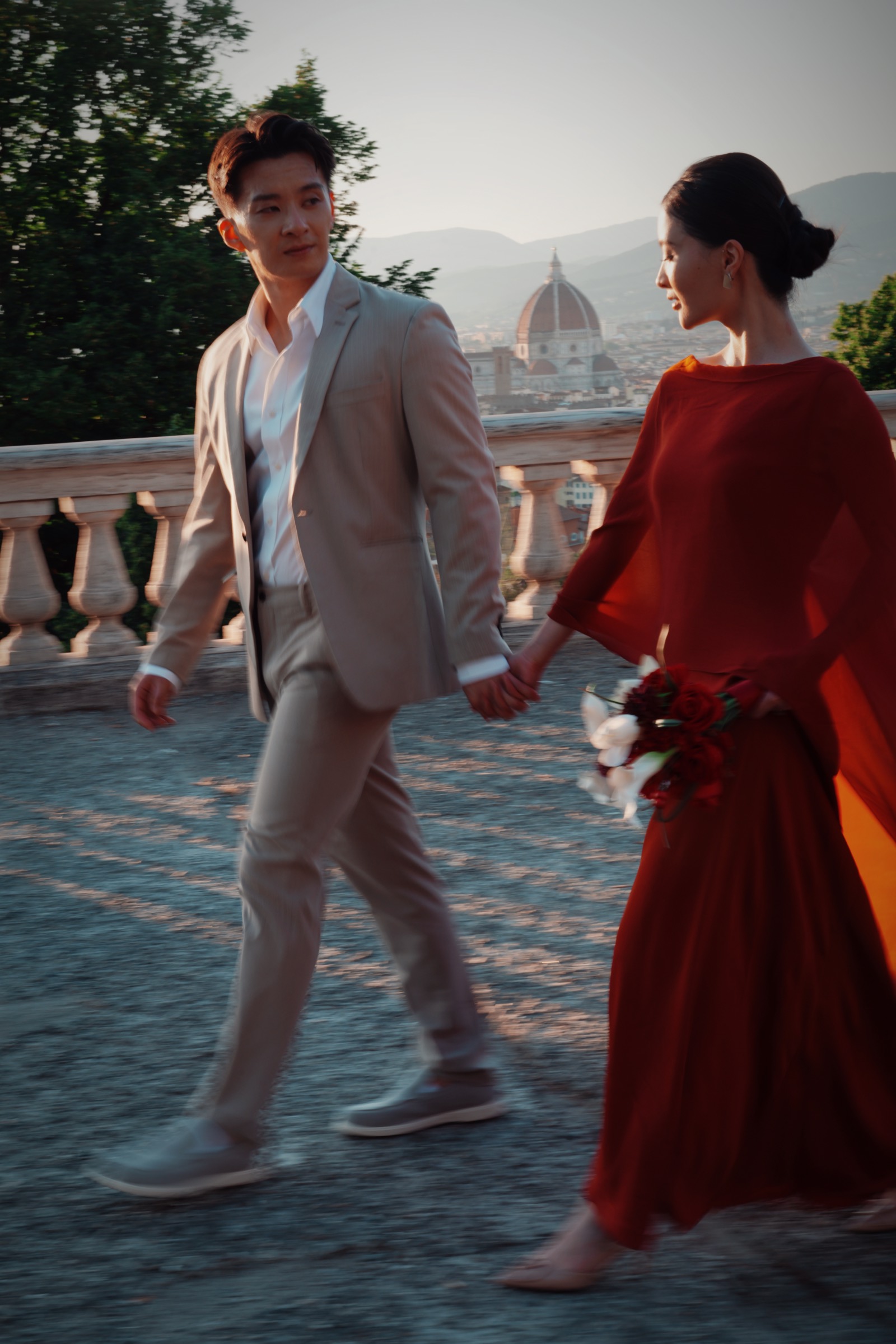 Yue and Andrew walking hand in hand along a terrace above Florence at sunset