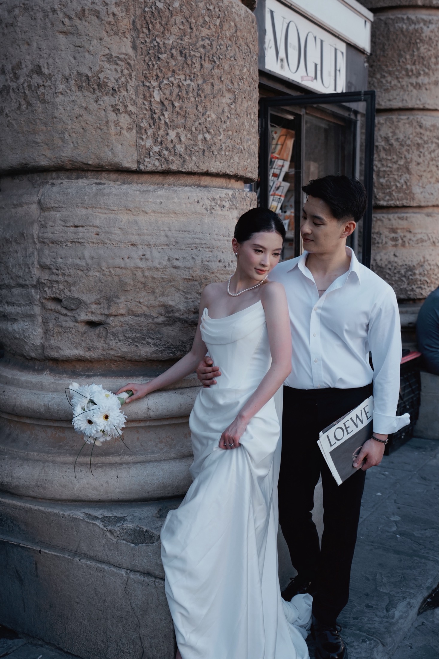 Yue and Andrew leaning against a stone column beside a newsstand